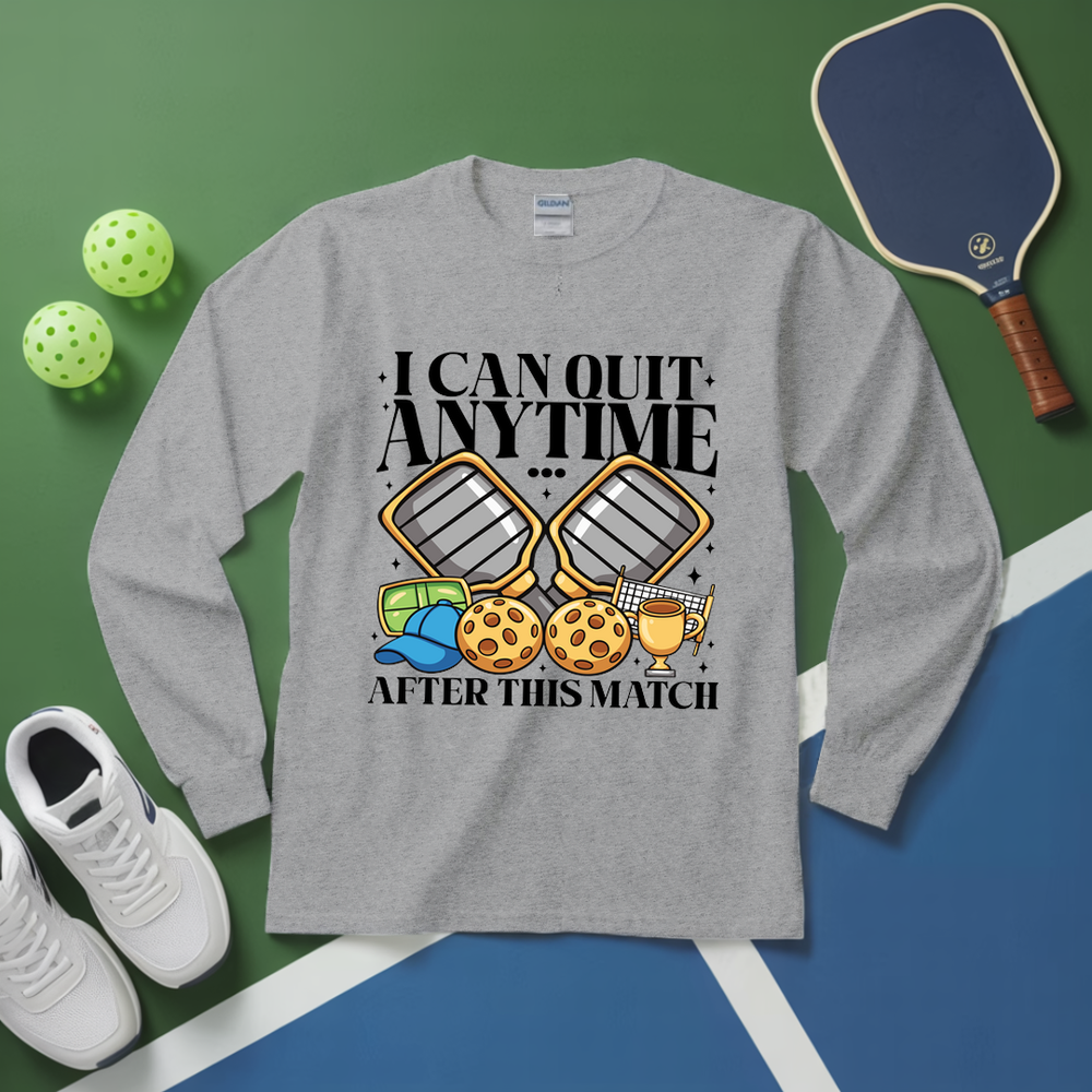Gray long-sleeve shirt with pickleball-themed design on a green and blue surface with pickleballs and a paddle.