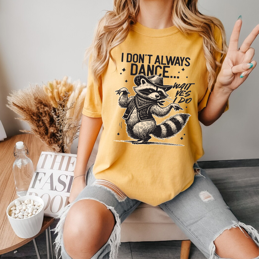 Person wearing a yellow t-shirt with a raccoon graphic and text, sitting in a casual setting.