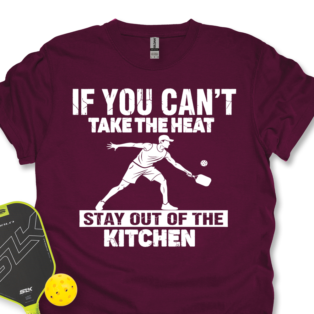 Maroon t-shirt with white text and pickleball player graphic, accompanied by a pickleball paddle and ball on a white background.