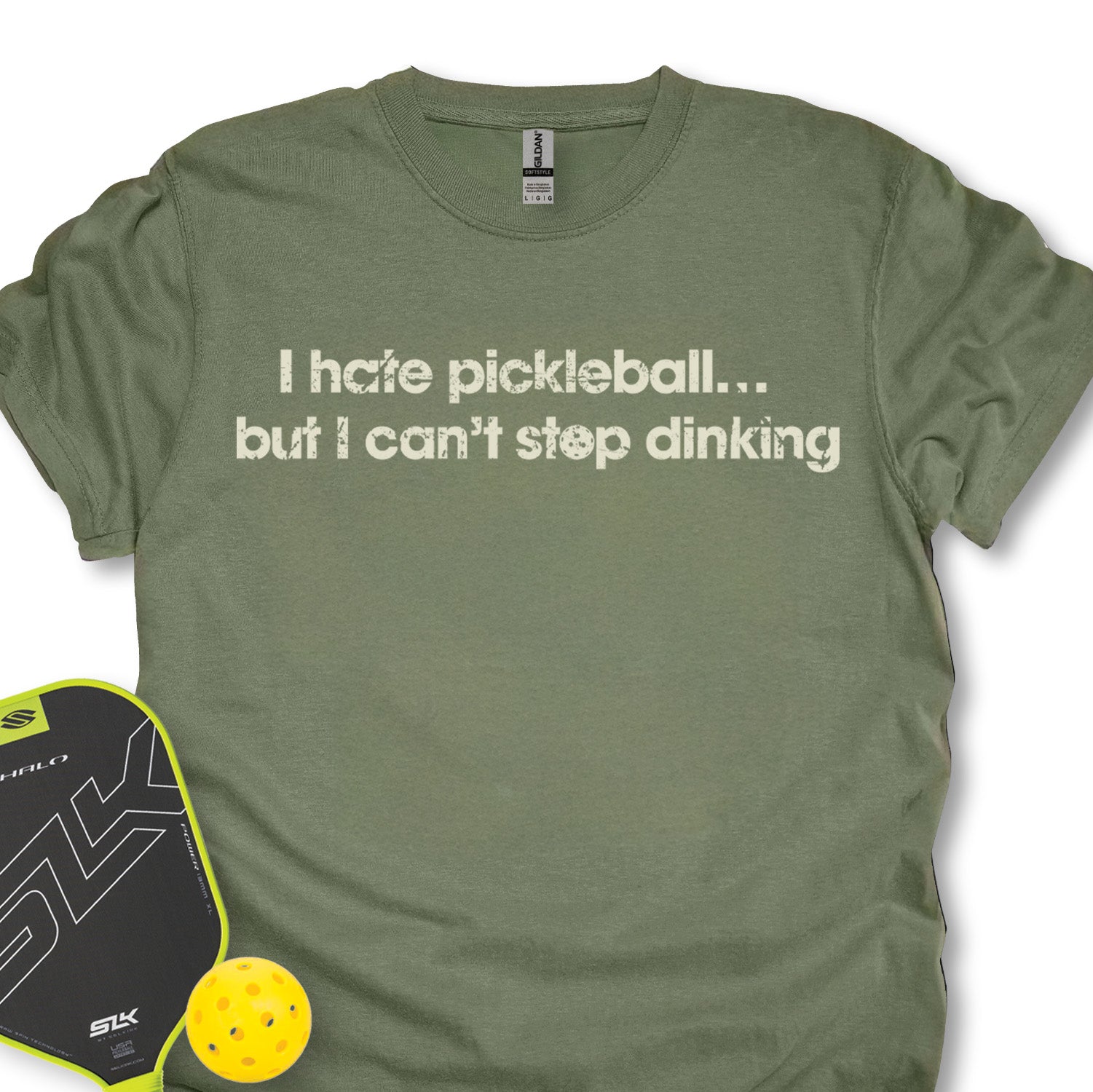 Green t-shirt with humorous pickleball text, next to a pickleball paddle and ball on a white background