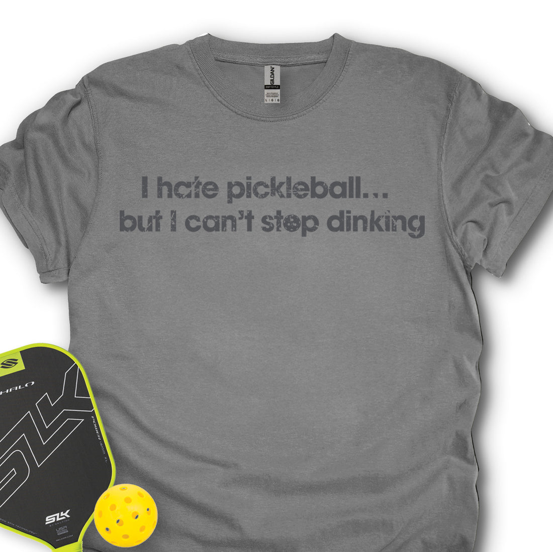 Gray t-shirt with humorous pickleball text, next to a pickleball paddle and ball on a white background