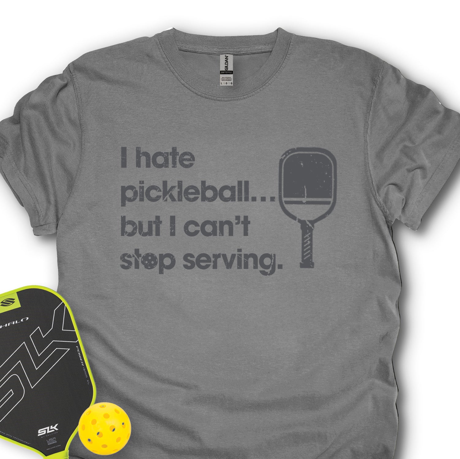 Gray t-shirt with humorous pickleball text and paddle graphic, next to a pickleball paddle and ball.