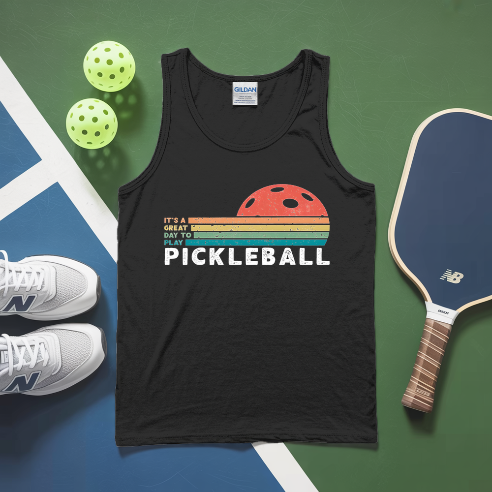 White tank top with pickleball design, pickleballs, and paddle on a green and blue surface