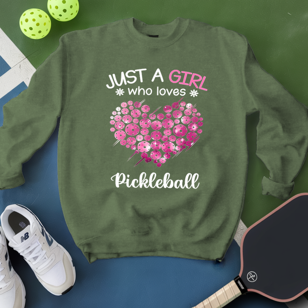 Green sweatshirt with pink heart design and text 'Just a girl who loves Pickleball' on a blue surface with pickleball equipment.