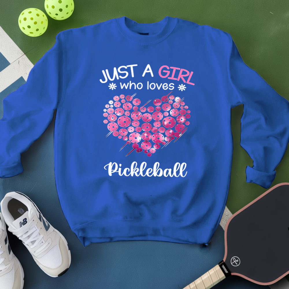 Blue sweatshirt with pink floral heart and text 'Just a girl who loves Pickleball' on a green surface with pickleball equipment.
