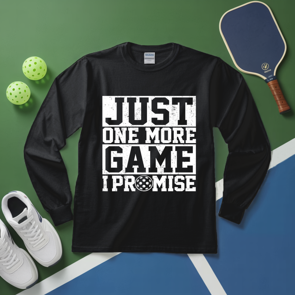 Black long-sleeve shirt with 'Just One More Game I Promise' text on a sports-themed background with pickleball equipment.