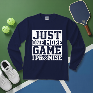 Navy blue sweatshirt with 'Just One More Game I Promise' text on a green and blue surface with pickleball equipment.