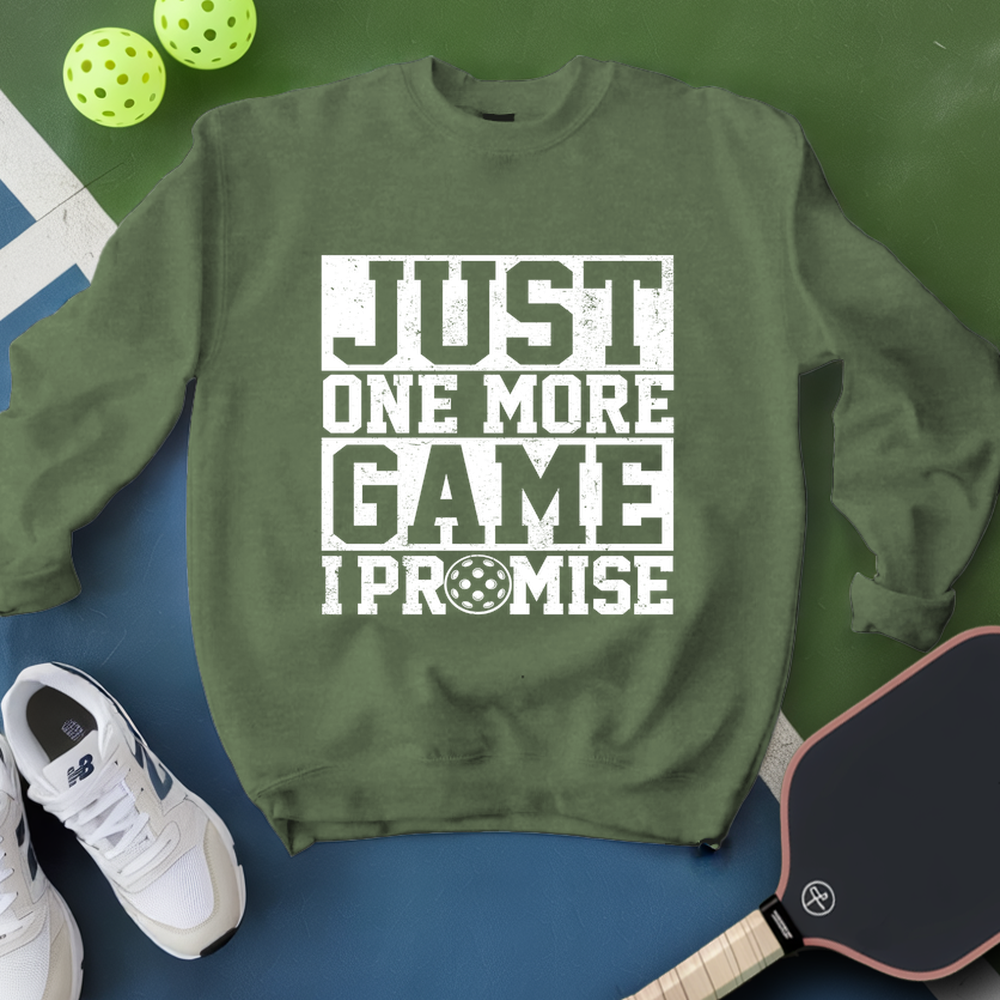 Green sweatshirt with 'Just One More Game I Promise' text, white sneakers, pickleball paddle, and balls on a green and blue background.