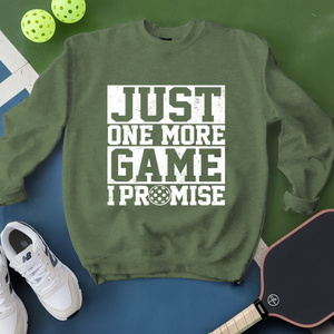 Green sweatshirt with 'Just One More Game I Promise' text, white sneakers, pickleball paddle, and balls on a green and blue background.