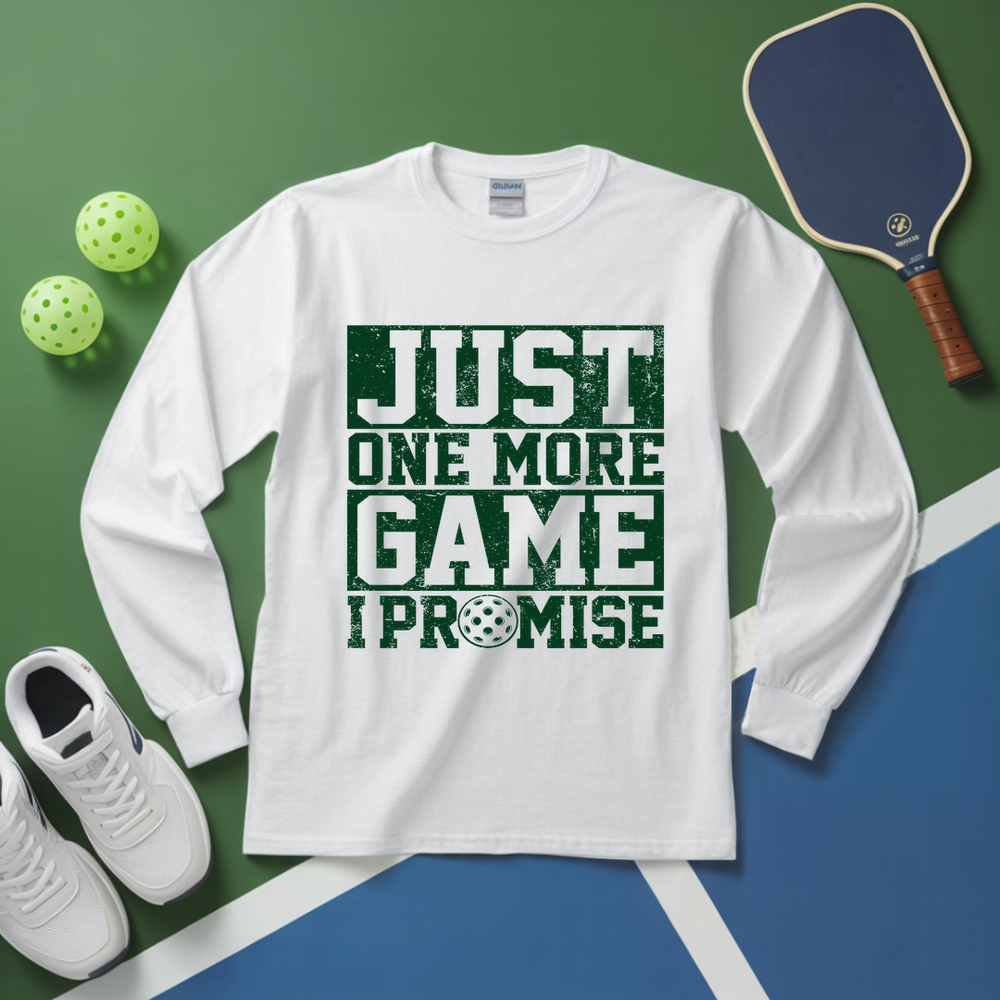 White long-sleeve shirt with 'Just One More Game I Promise' text on a green and blue background with pickleball equipment.