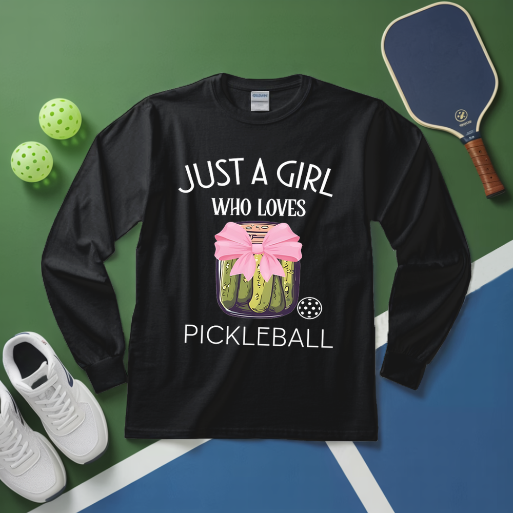 Black long-sleeve shirt with pickleball design and text on a green and blue surface with pickleball equipment.