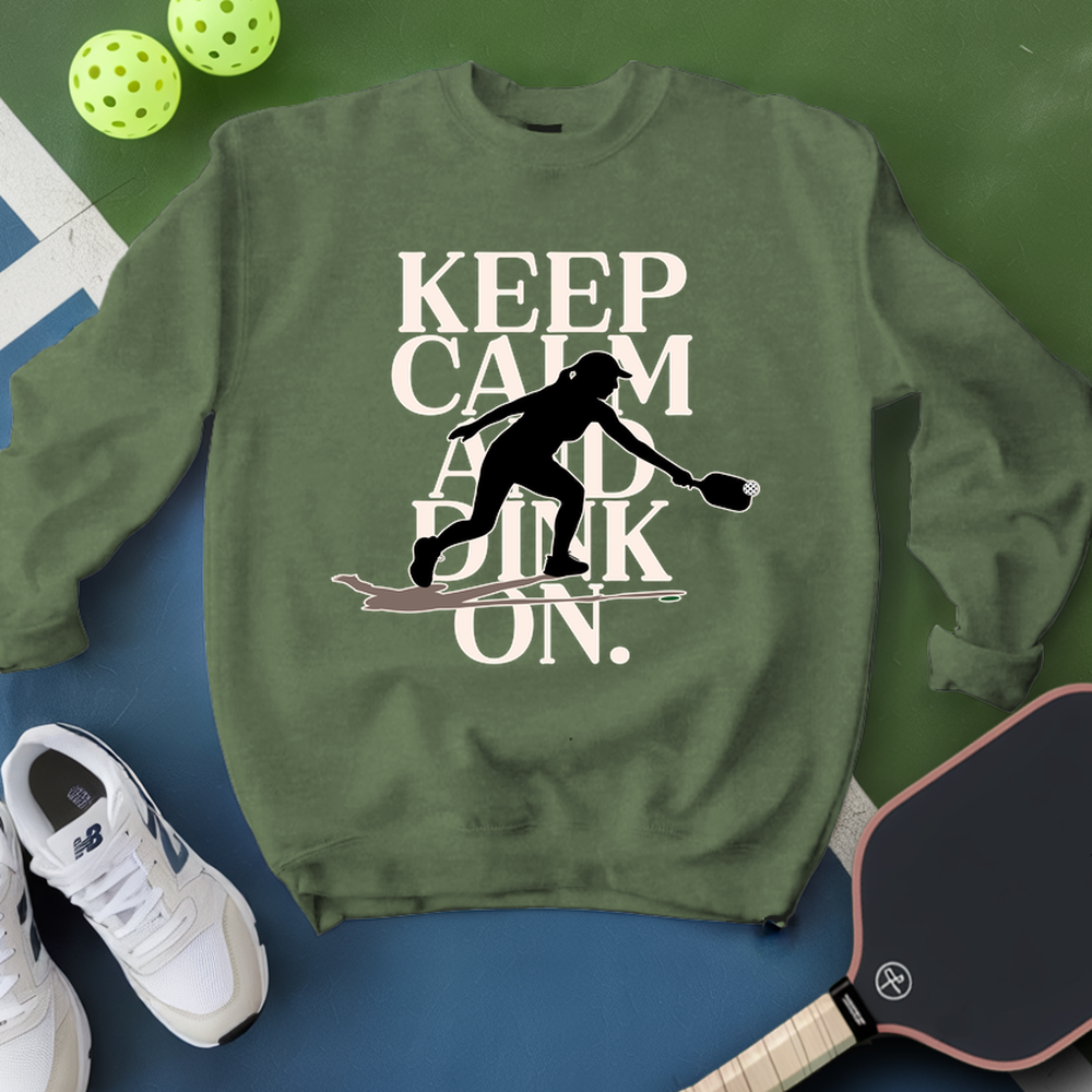 Green sweatshirt with 'Keep Calm and Pickle On' text and silhouette, next to pickleball equipment on a green and blue background.