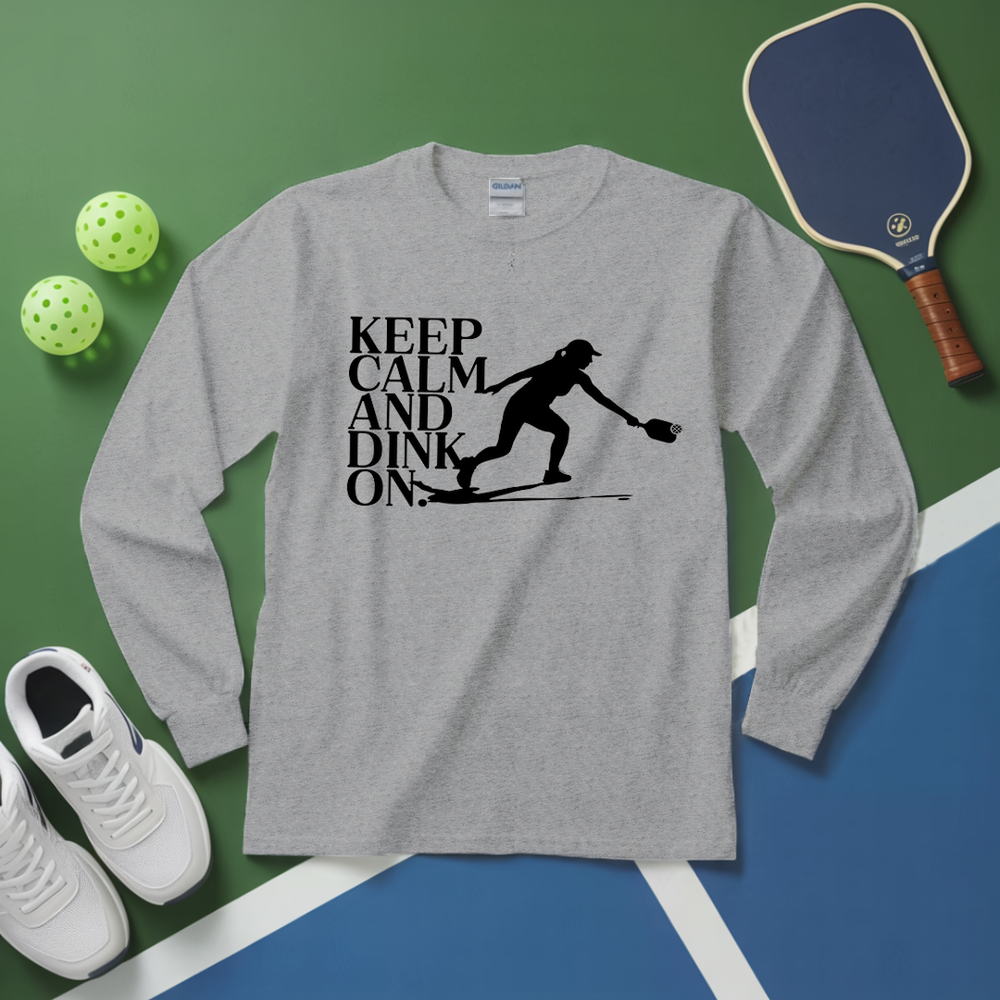 Gray long-sleeve shirt with 'Keep Calm and Dink On' graphic on a green and blue surface with pickleball equipment.