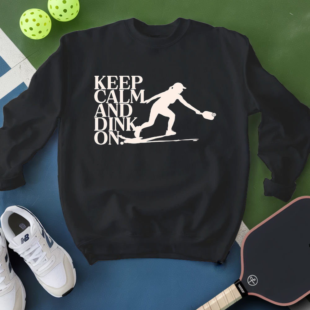 Black sweatshirt with 'Keep Calm and Dink On' graphic on a blue and green background with pickleball equipment.