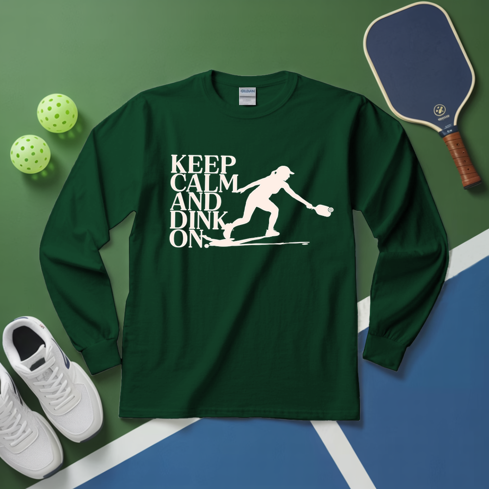 Green long-sleeve shirt with 'Keep Calm and Dink On' graphic on a green and blue surface with pickleball equipment.