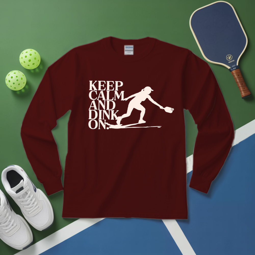 Maroon long-sleeve shirt with 'Keep Calm and Dink On' graphic on a green and blue surface with pickleball equipment.