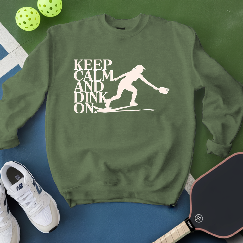 Green sweatshirt with 'Keep Calm and Dink On' text and pickleball player graphic, surrounded by pickleballs and a paddle.