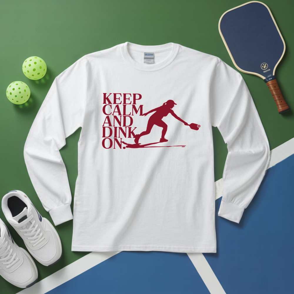 White long-sleeve shirt with 'Keep Calm and Dink On' graphic on a green and blue background with pickleball equipment.