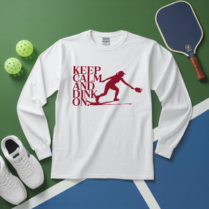 White long-sleeve shirt with 'Keep Calm and Dink On' graphic on a green and blue background with pickleball equipment.