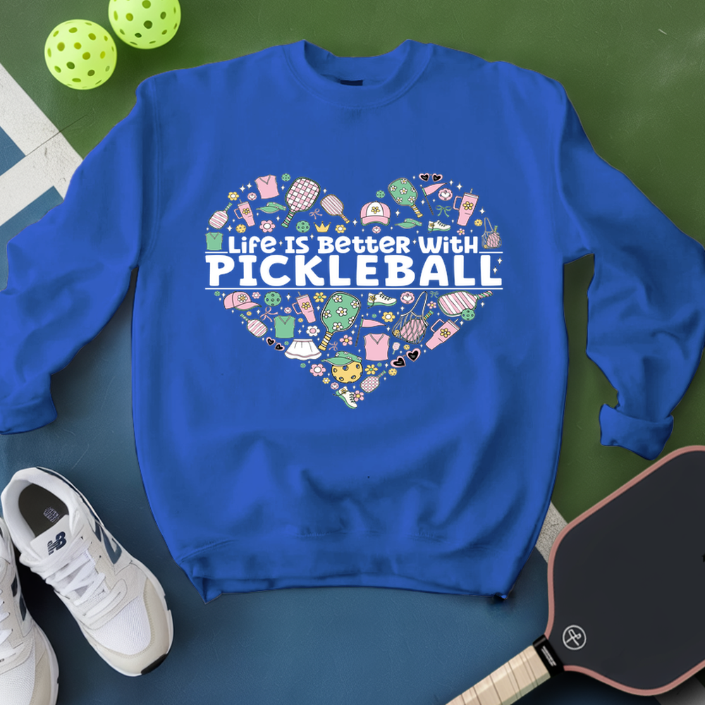 Blue sweatshirt with pickleball-themed design on a green surface with pickleballs and a paddle.