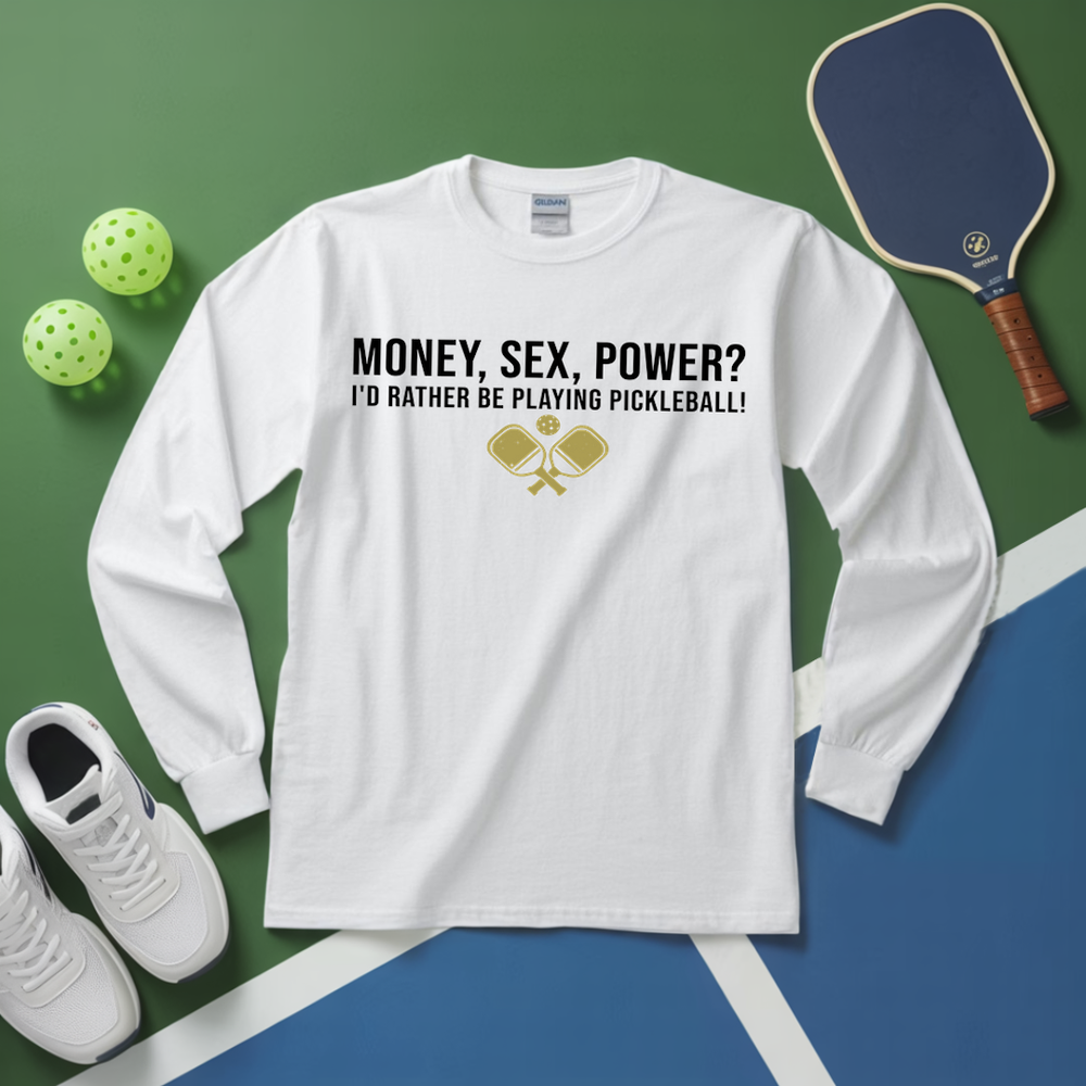 White long-sleeve shirt with pickleball-themed text and graphics on a green and blue surface with pickleball equipment.