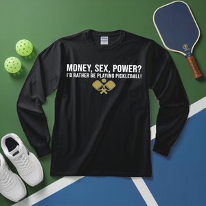 Black long-sleeve shirt with pickleball-themed text on a green and blue surface with pickleball equipment.