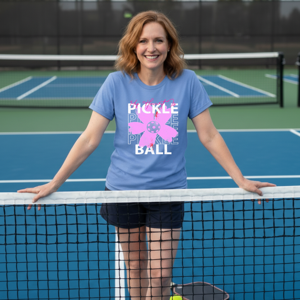 Woman wearing a blue t-shirt with a pink flower design and text on a tennis court.