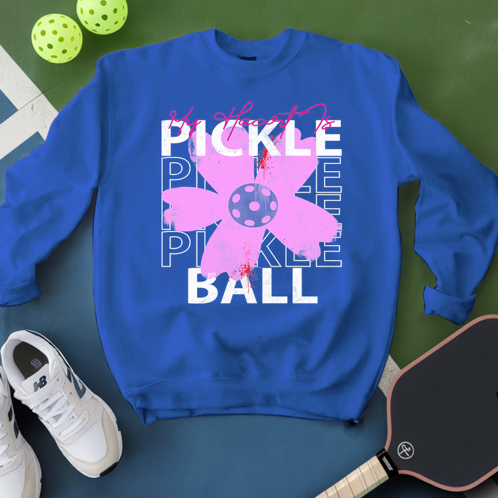 Blue sweatshirt with pickleball design on a green surface with pickleballs and a paddle.