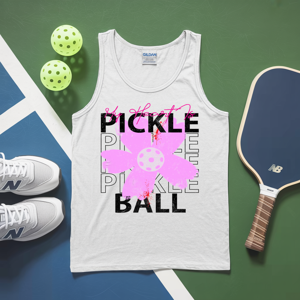 White tank top with pickleball design, pickleballs, and paddle on a green and blue surface