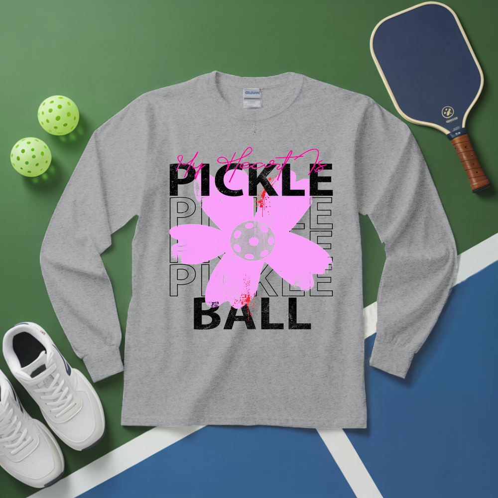Gray long-sleeve shirt with pickleball-themed design on a green and blue surface with pickleball equipment.