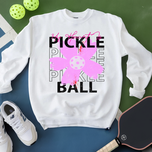 White sweatshirt with pickleball-themed design on a green and blue surface with pickleballs and a paddle.