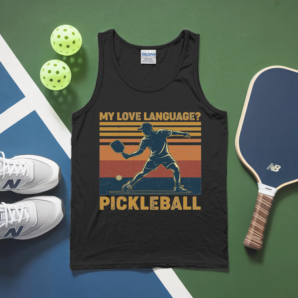 Black tank top with pickleball graphic and text, surrounded by pickleballs, shoes, and paddle on a green and blue surface.