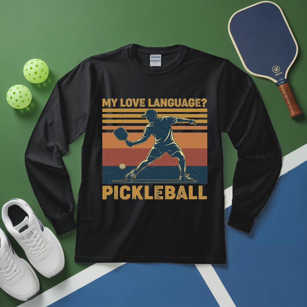 Black long-sleeve shirt with pickleball graphic and text on a green and blue surface with pickleball equipment.