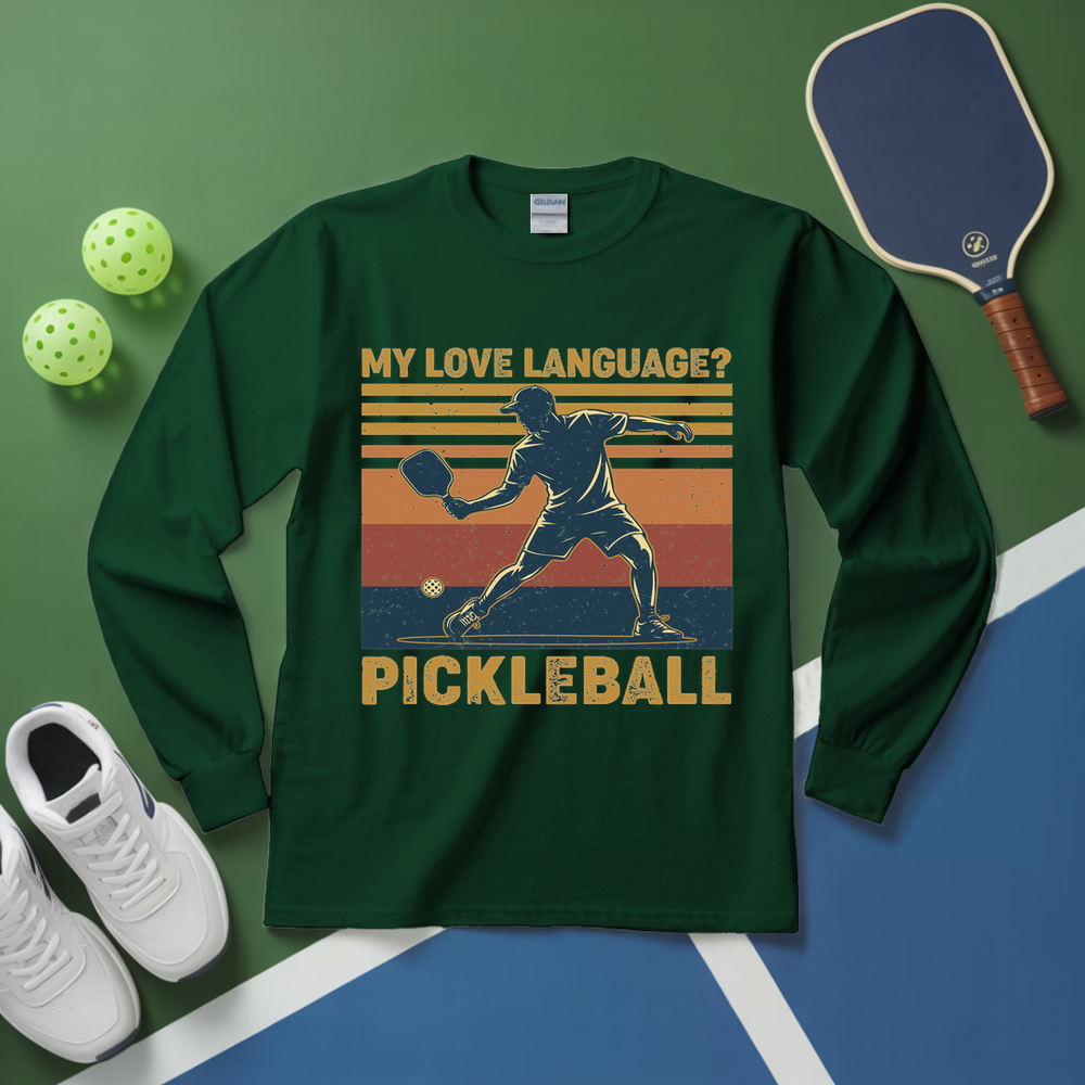 Green long-sleeve shirt with pickleball graphic and text on a green and blue surface with pickleball equipment.