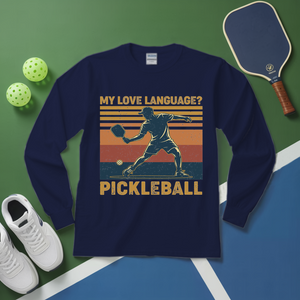 Navy blue long-sleeve shirt with pickleball graphic and text on a green and blue surface with pickleballs and paddle.