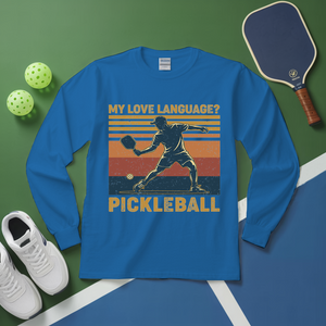 Blue long-sleeve shirt with pickleball graphic and text on a green and blue surface with pickleball equipment.