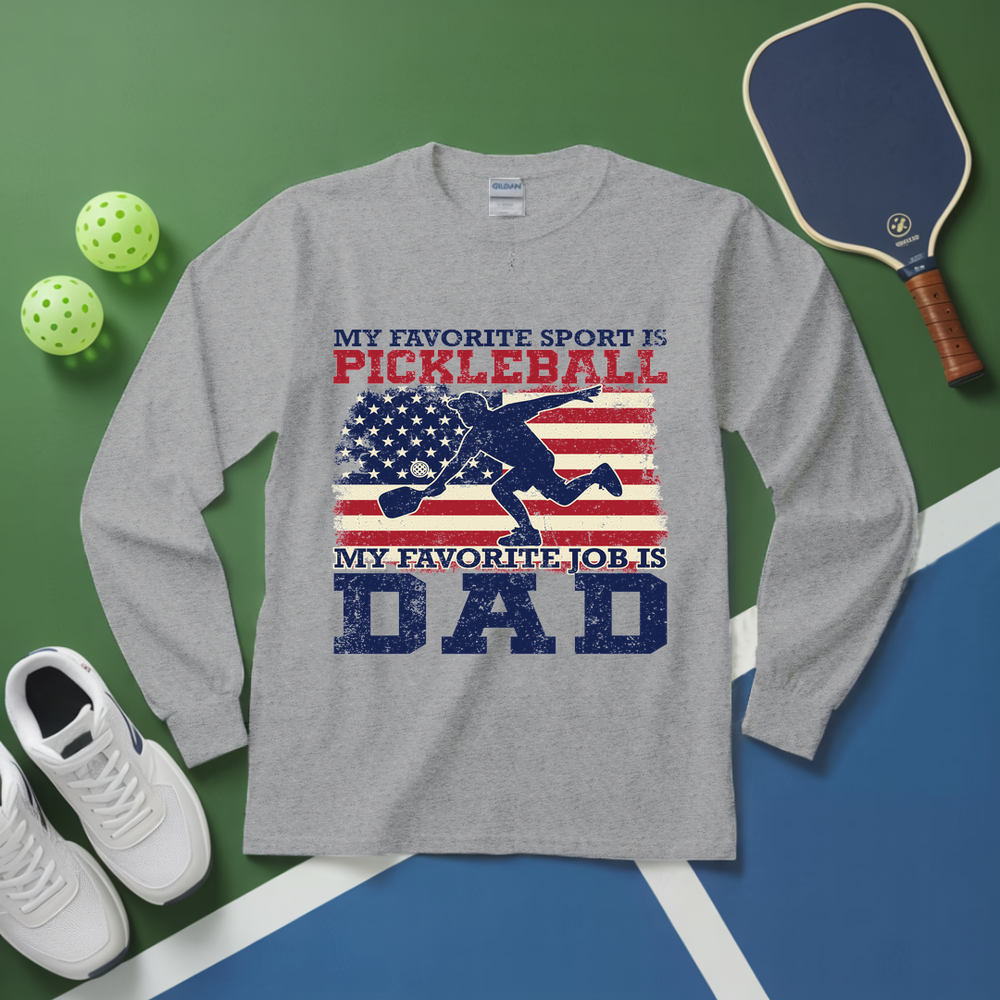 Gray long-sleeve shirt with pickleball-themed design on a green and blue surface with pickleball equipment.