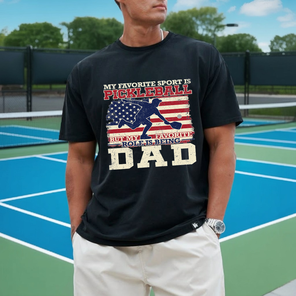 Person wearing a black t-shirt with pickleball-themed text on a tennis court