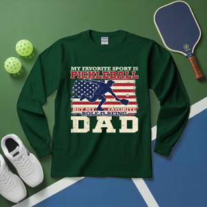 Green long-sleeve shirt with pickleball design and text on a green and blue surface with pickleball equipment.