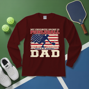 Maroon long-sleeve shirt with pickleball design and text on a green and blue surface with pickleball equipment.