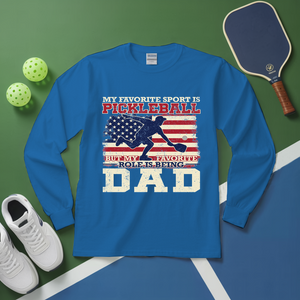 Blue long-sleeve shirt with pickleball design and text on a green and blue surface with pickleball equipment.