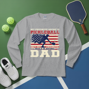 Gray long-sleeve shirt with pickleball-themed design on a green and blue surface with pickleball equipment.