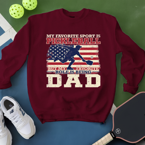 Maroon sweatshirt with pickleball design and text on a green and blue background