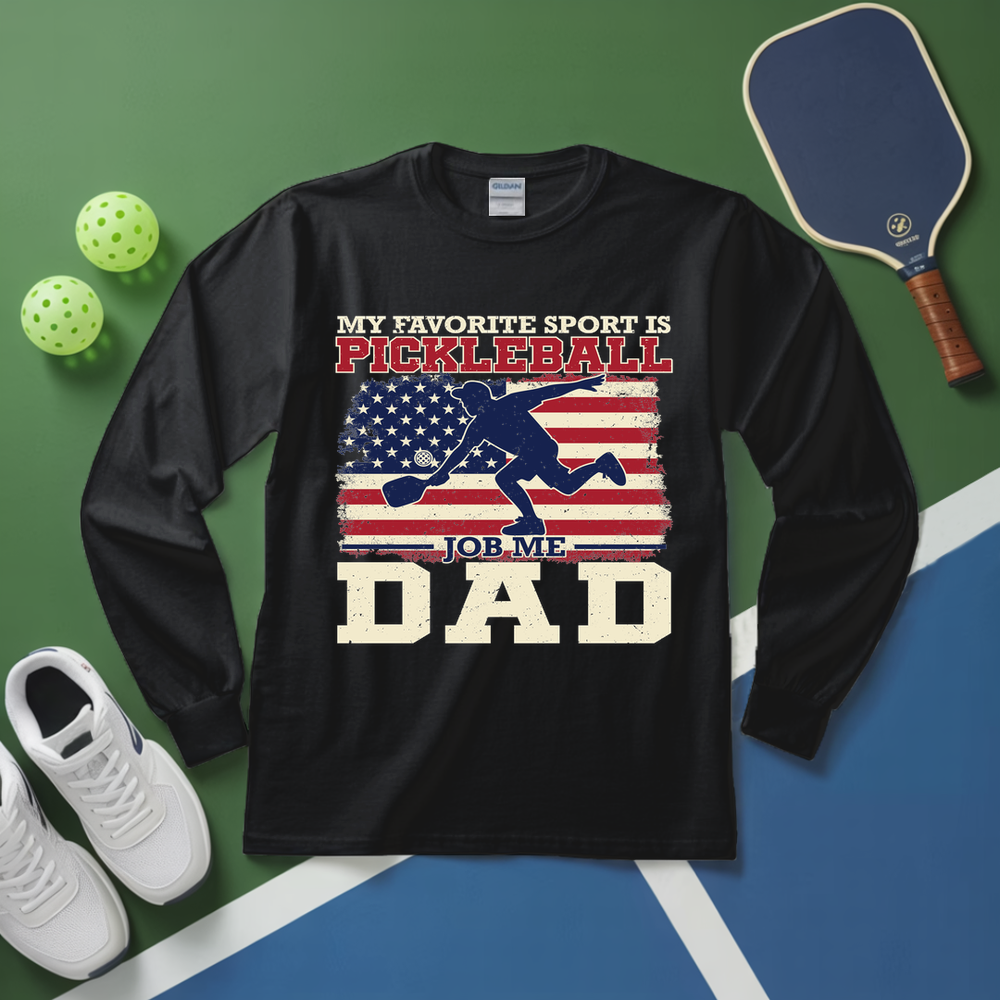 Black long-sleeve shirt with pickleball-themed design on a green and blue surface with pickleball equipment.