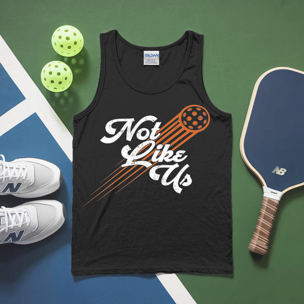 Black tank top with 'Not Like Us' design, pickleball paddles, and balls on a green and blue background