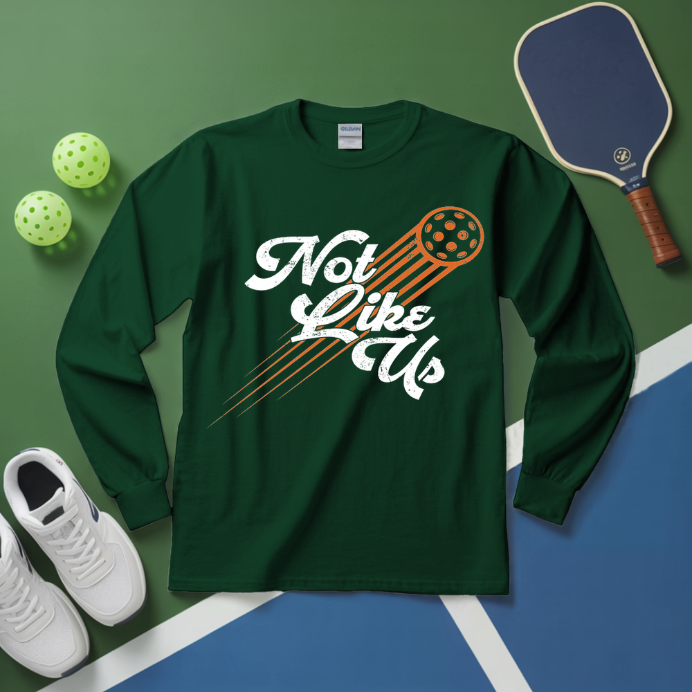Green long-sleeve shirt with 'Not Like Us' design on a green and blue surface with pickleball equipment.