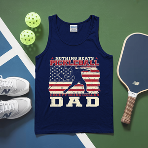 Navy tank top with pickleball design and text, placed on a green and blue surface with pickleballs and a paddle.