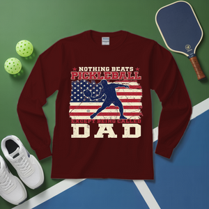 Maroon long-sleeve shirt with pickleball design and text on a green and blue surface with pickleball equipment.