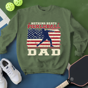 Green sweatshirt with pickleball design and text, surrounded by pickleballs and a paddle on a green and blue background.
