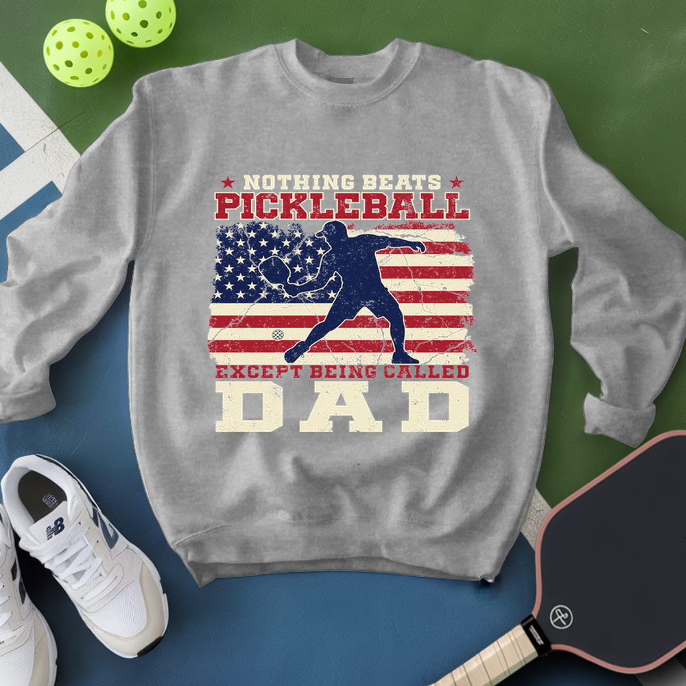 Gray sweatshirt with pickleball design and text, surrounded by pickleballs and a paddle on a green and blue background.
